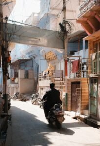 A person rides a scooter down a narrow street.